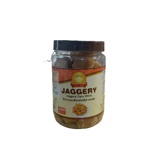A jar of Soghn Jaggery Cube White (Rohrzuckerwärfel weiÿ) placed on a light wooden table in a store setting, with shelves and other products visible in the background.